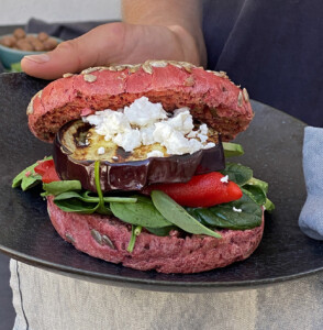 A photograph of Bodhi's Beetroot Spelt Flour Sourdough Bun filled with spinach, roast eggplant, roast capsicum, spinach and feta on a serving plate